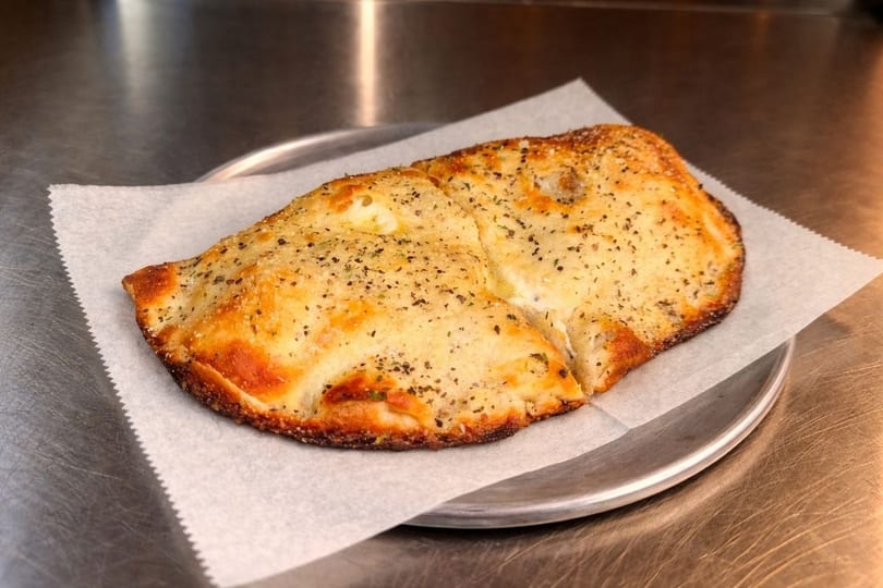 Golden brown calzone with herbs and spices on parchment paper, on a metal tray.