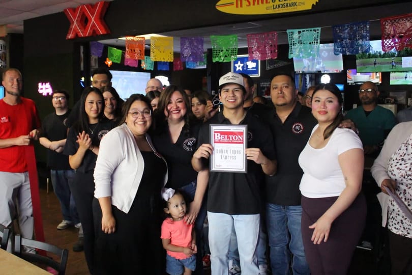 A group of people, including a child, smiling and posing with a "Belton" certificate in a restaurant.