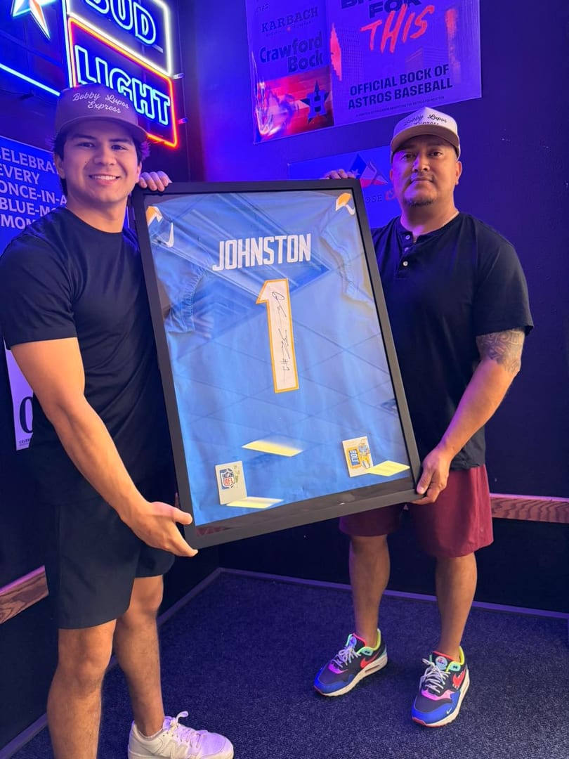 Two men holding a framed blue sports jersey with "JOHNSTON" and the number "1" on it.