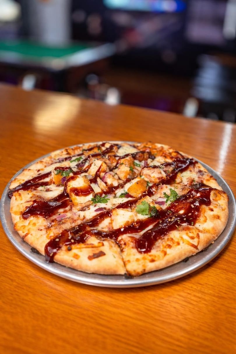 BBQ chicken pizza with red onions and cilantro on a metal tray on a wooden bar.
